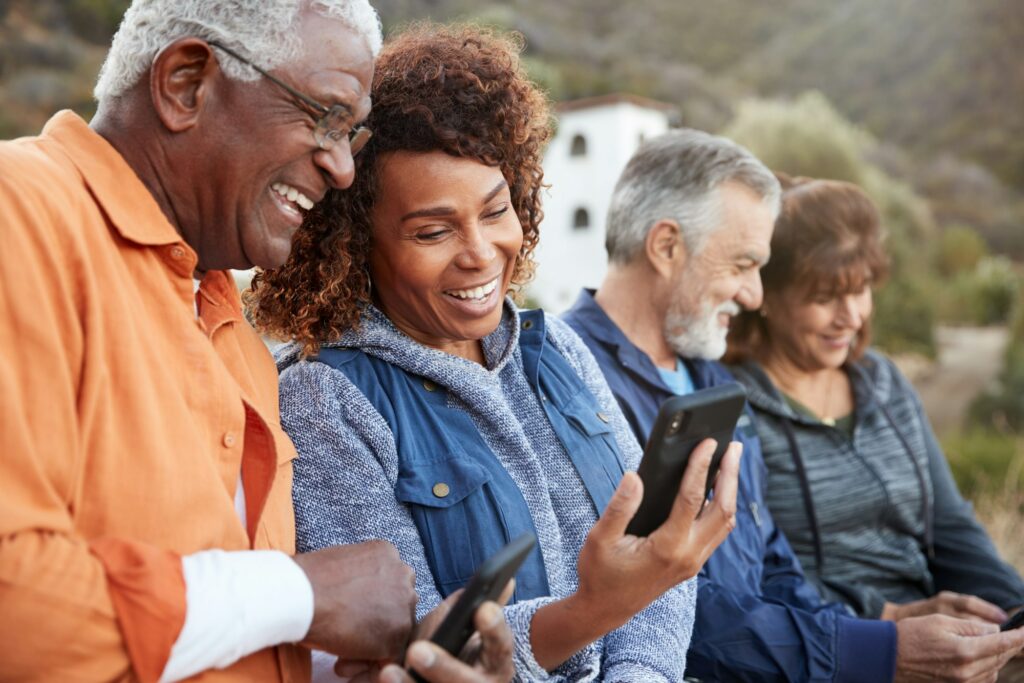 Group Of Senior Friends On Hike In Countryside Looking At Mobiles Phones Together